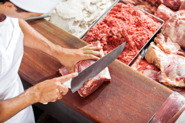 High angle portrait of smiling butcher cutting meat at counter in butchery